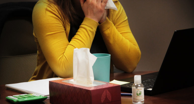 Woman sitting at a desk blowing her nose.